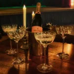 Eine Flasche Champagner in einem Kühler mit vier eleganten Gläsern auf einem Holztisch.